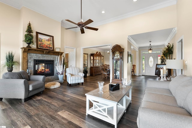 living room with crown molding, a stone fireplace, dark hardwood / wood-style floors, and a towering ceiling