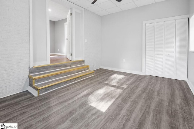 interior space featuring dark wood-type flooring, ceiling fan, brick wall, a drop ceiling, and a closet