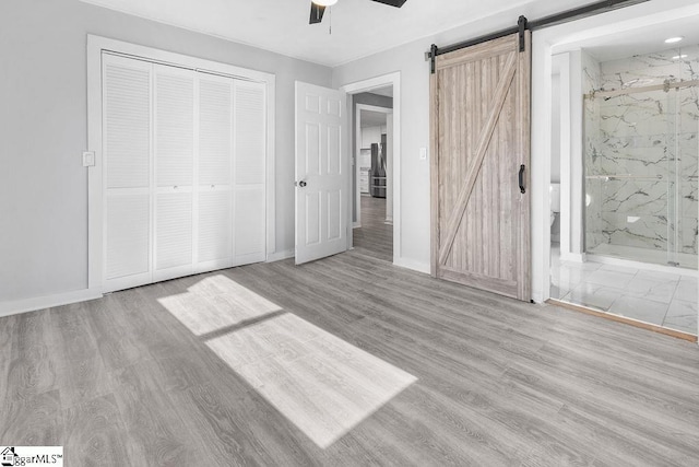 unfurnished bedroom with ensuite bath, light hardwood / wood-style flooring, a closet, ceiling fan, and a barn door