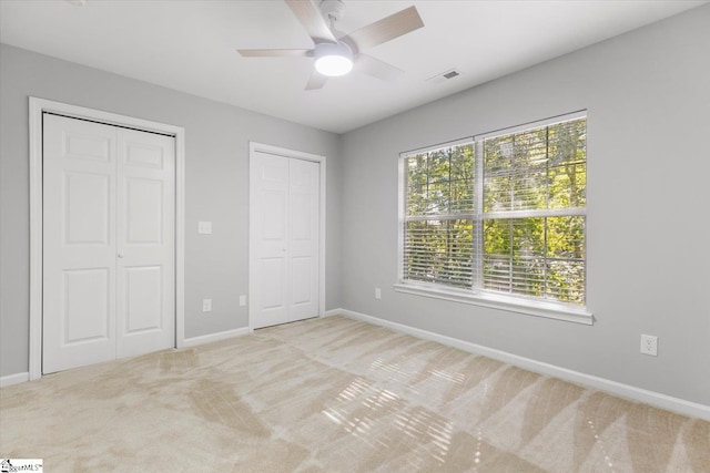 unfurnished bedroom featuring multiple closets, light carpet, and ceiling fan