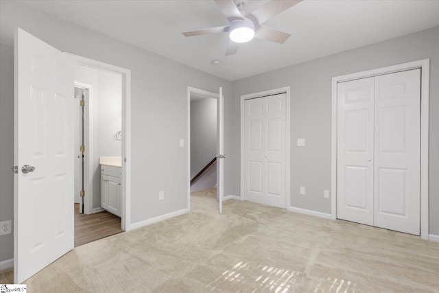 unfurnished bedroom featuring ensuite bath, two closets, light colored carpet, and ceiling fan