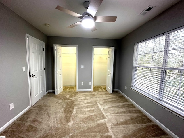 unfurnished bedroom with a walk in closet, light colored carpet, and ceiling fan