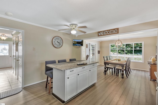 kitchen with white cabinets, a kitchen bar, light wood-type flooring, pendant lighting, and light stone counters