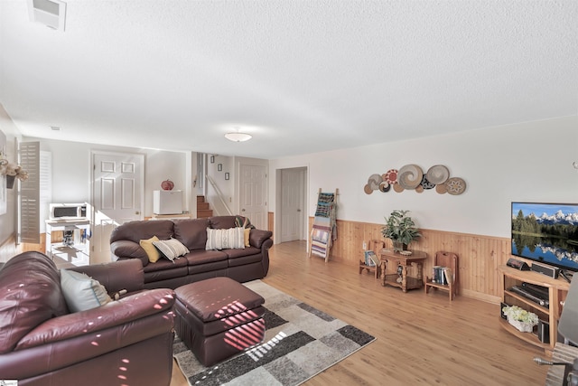 living room featuring wood walls, a textured ceiling, and light wood-type flooring