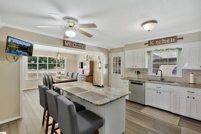 kitchen featuring dishwasher, sink, plenty of natural light, white cabinets, and light stone counters