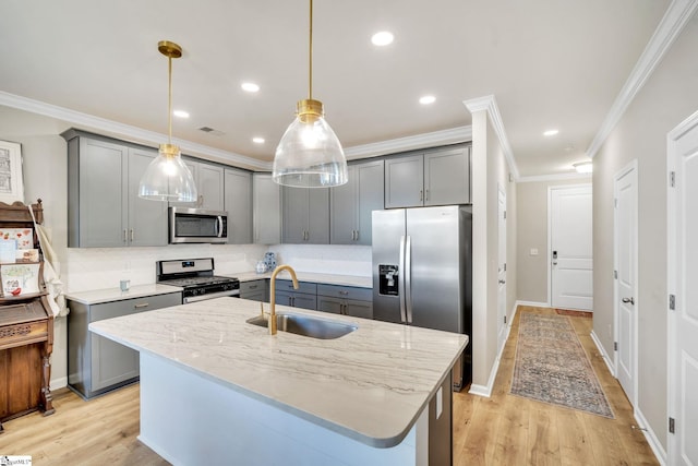 kitchen featuring hanging light fixtures, an island with sink, appliances with stainless steel finishes, light wood-type flooring, and sink