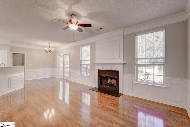 unfurnished living room with crown molding, light hardwood / wood-style flooring, a textured ceiling, and ceiling fan with notable chandelier