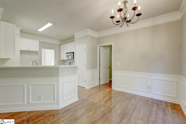 kitchen featuring ornamental molding, white cabinets, a notable chandelier, and light wood-type flooring