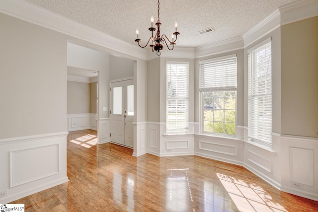 unfurnished dining area with a chandelier, a textured ceiling, crown molding, and light hardwood / wood-style floors