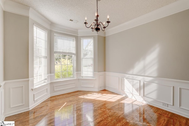 empty room featuring an inviting chandelier, ornamental molding, a textured ceiling, and light wood-type flooring