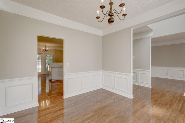 unfurnished room featuring crown molding, a notable chandelier, a textured ceiling, and light wood-type flooring