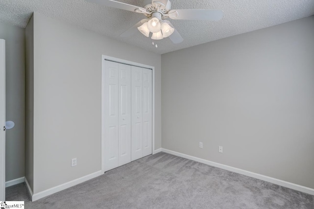 unfurnished bedroom featuring light colored carpet, a textured ceiling, a closet, and ceiling fan