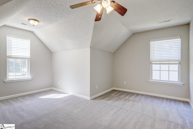 additional living space featuring vaulted ceiling, light carpet, a textured ceiling, and ceiling fan