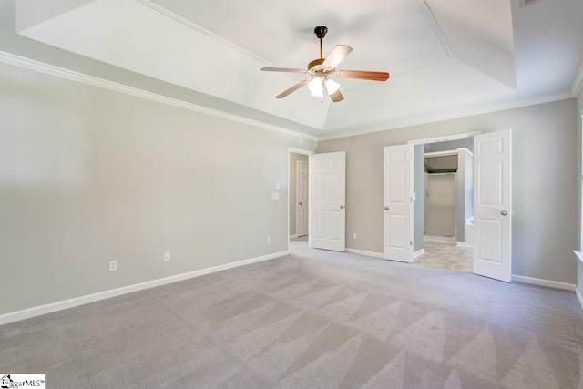 unfurnished bedroom featuring a raised ceiling, a closet, ceiling fan, crown molding, and light colored carpet