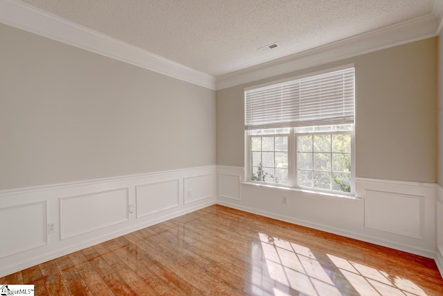 empty room with ornamental molding, light hardwood / wood-style flooring, and a textured ceiling