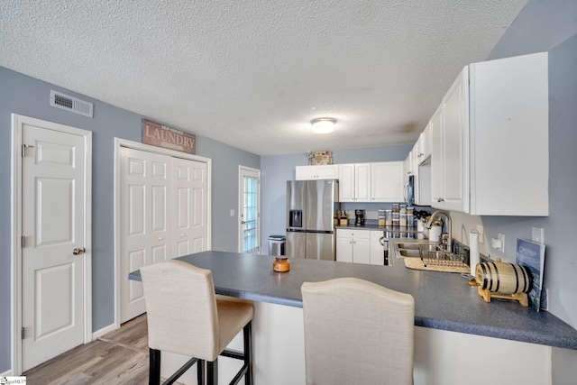 kitchen featuring kitchen peninsula, white cabinetry, a kitchen bar, light wood-type flooring, and stainless steel appliances