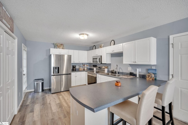 kitchen with light wood-type flooring, appliances with stainless steel finishes, kitchen peninsula, and white cabinets