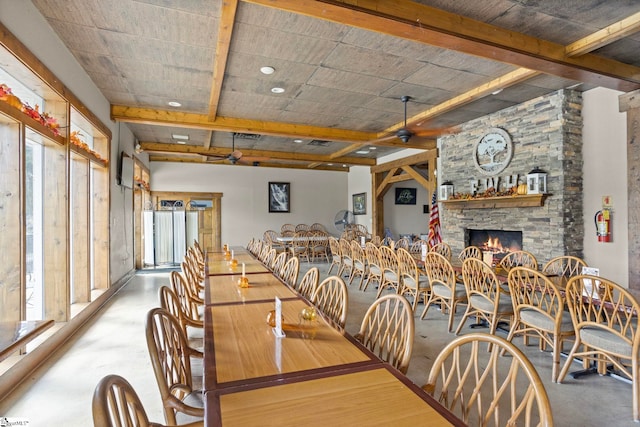 dining space featuring ceiling fan, a wealth of natural light, a stone fireplace, and concrete floors