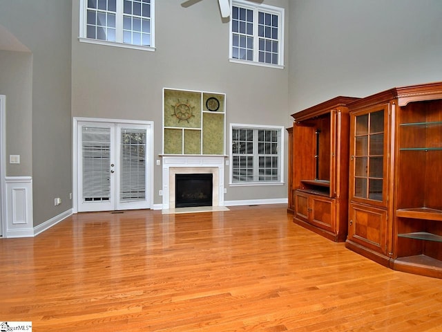 unfurnished living room with light hardwood / wood-style flooring, french doors, a high ceiling, and ceiling fan