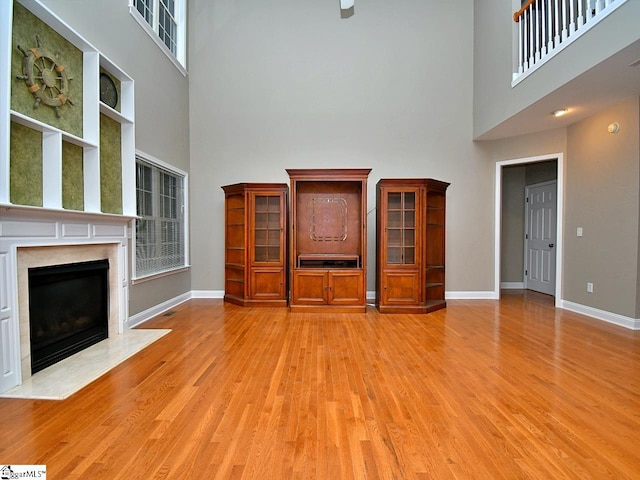 unfurnished living room with light hardwood / wood-style flooring, a high ceiling, and a fireplace