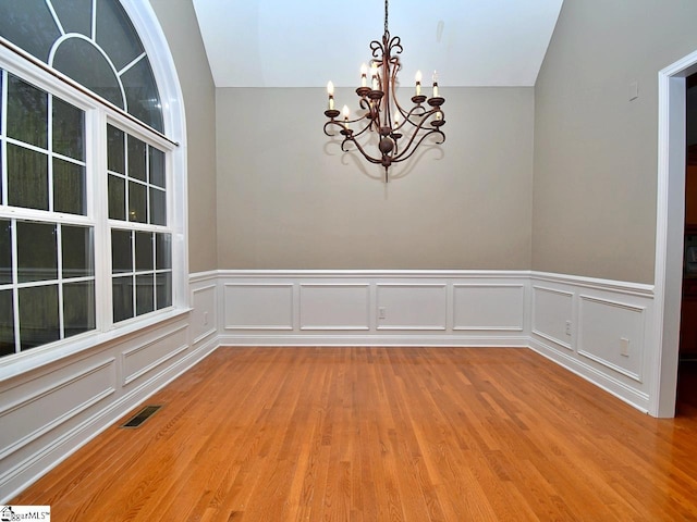 empty room with a notable chandelier, lofted ceiling, and light hardwood / wood-style flooring