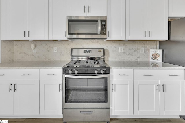 kitchen featuring appliances with stainless steel finishes, white cabinets, light stone counters, and backsplash