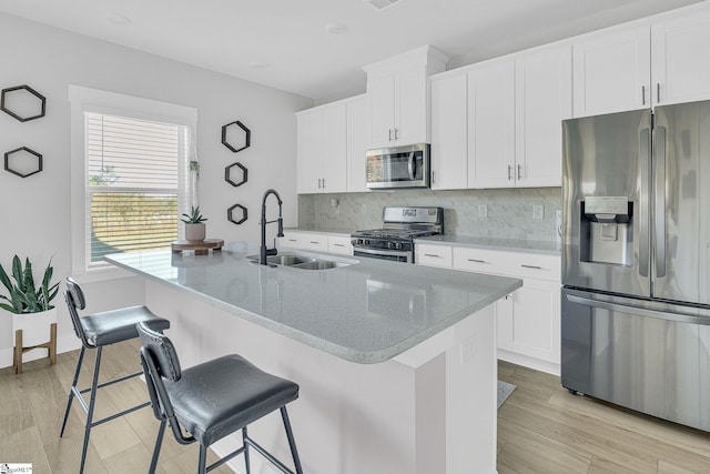 kitchen with stainless steel appliances, light wood-type flooring, a center island with sink, and white cabinets