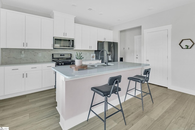 kitchen featuring a kitchen island with sink, a kitchen breakfast bar, light hardwood / wood-style flooring, sink, and appliances with stainless steel finishes