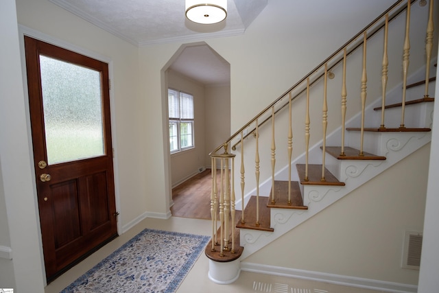 entrance foyer with arched walkways, visible vents, baseboards, stairs, and ornamental molding