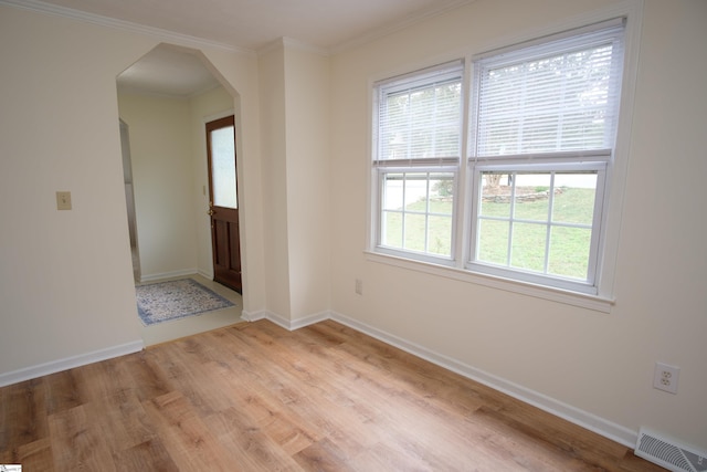 spare room featuring baseboards, visible vents, arched walkways, ornamental molding, and light wood-style floors