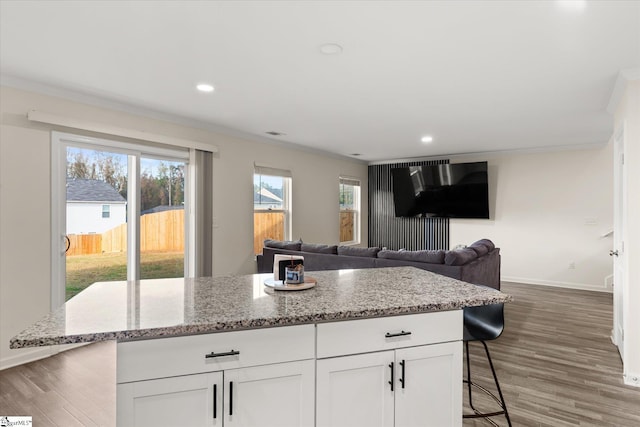 kitchen with a breakfast bar, white cabinetry, light stone countertops, and dark wood-type flooring