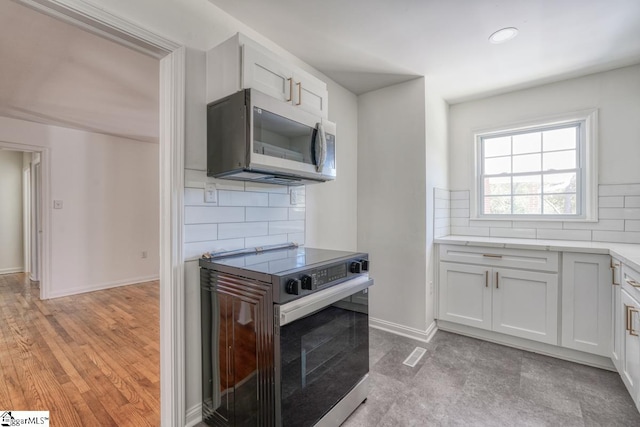 kitchen with light hardwood / wood-style floors, decorative backsplash, white cabinetry, and stainless steel appliances