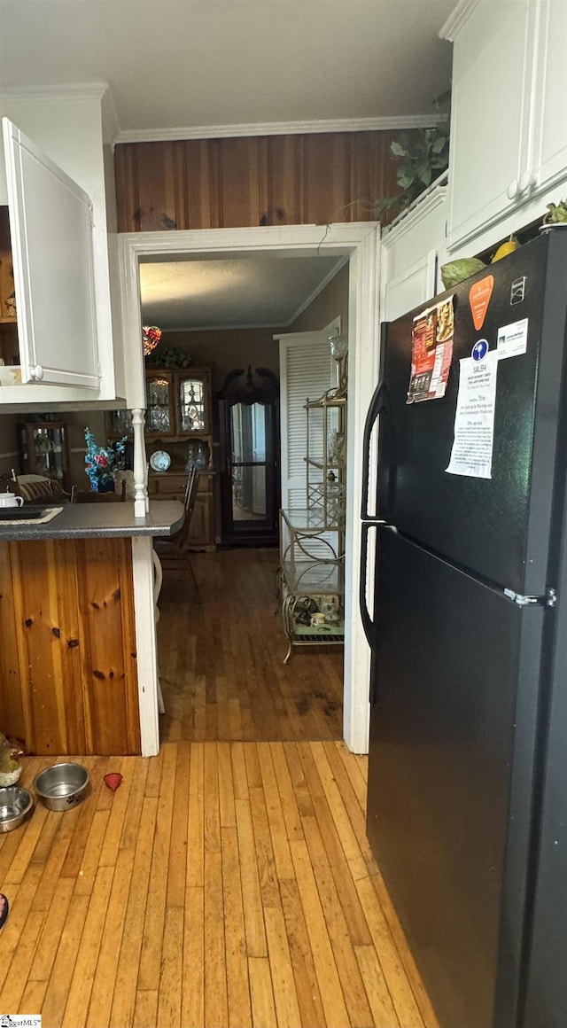 kitchen featuring white cabinets, light hardwood / wood-style floors, black fridge, and ornamental molding