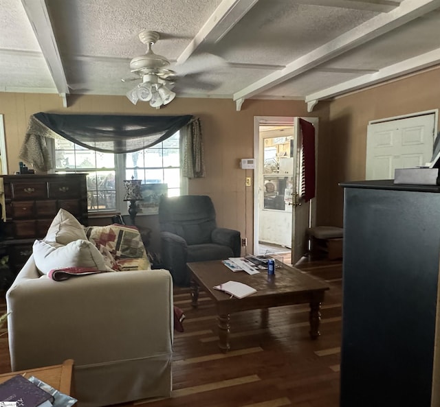 living area featuring a textured ceiling, ceiling fan, dark wood-type flooring, and beamed ceiling