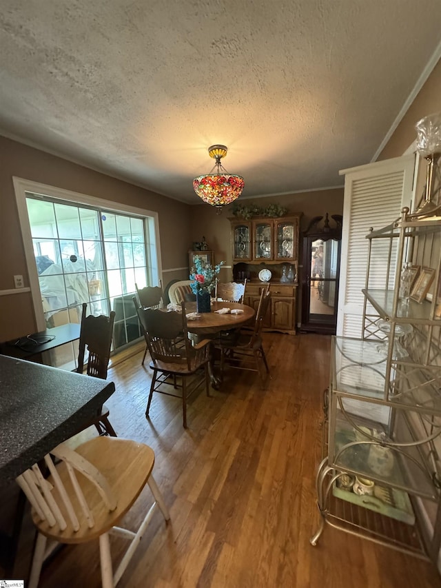 dining space with dark wood-type flooring, a textured ceiling, and ornamental molding