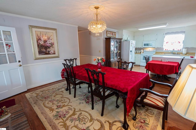 dining room with light hardwood / wood-style floors, an inviting chandelier, ornamental molding, and sink