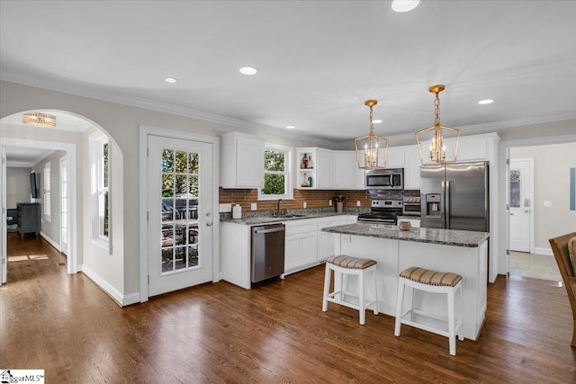 kitchen featuring a kitchen island, white cabinetry, stainless steel appliances, and dark stone countertops