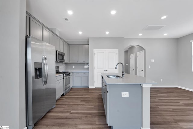 kitchen featuring an island with sink, appliances with stainless steel finishes, dark hardwood / wood-style floors, gray cabinets, and sink