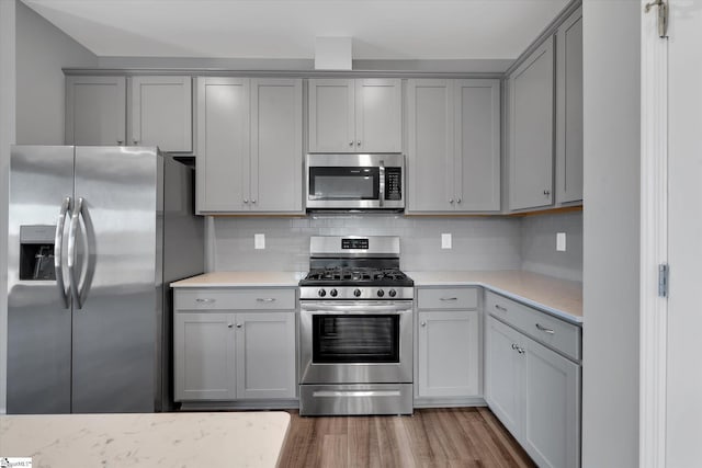 kitchen with gray cabinets, backsplash, stainless steel appliances, and wood-type flooring