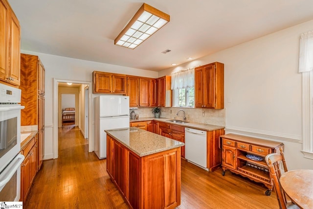 kitchen with white appliances, wood-type flooring, sink, a kitchen island, and backsplash