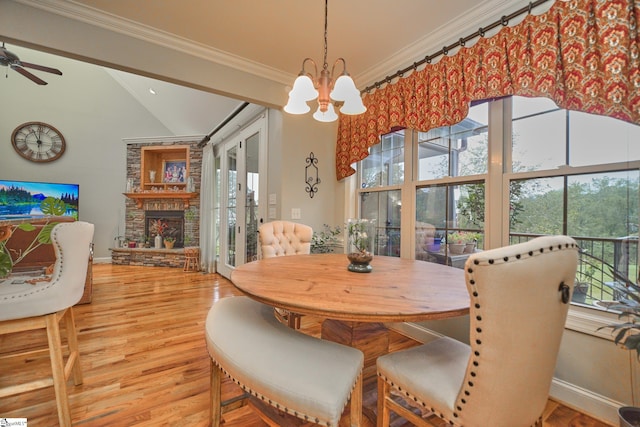 dining space featuring hardwood / wood-style flooring, vaulted ceiling, ceiling fan with notable chandelier, a fireplace, and crown molding