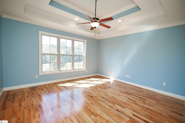 empty room featuring ornamental molding, ceiling fan, light wood-type flooring, and a raised ceiling