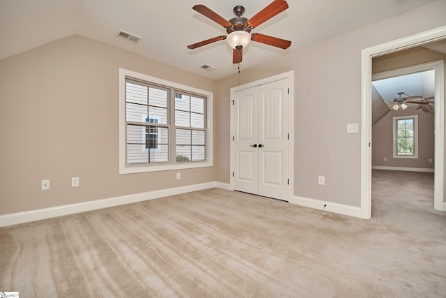 unfurnished bedroom with a closet, ceiling fan, vaulted ceiling, and light colored carpet