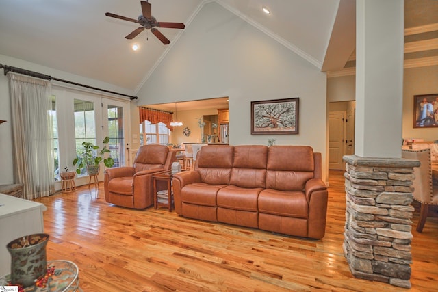 living room with light wood-type flooring, ceiling fan with notable chandelier, decorative columns, crown molding, and high vaulted ceiling