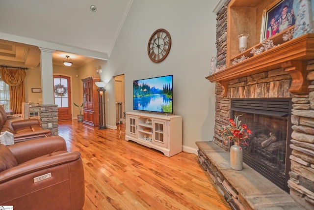 living room with ornamental molding, decorative columns, light hardwood / wood-style flooring, and a stone fireplace