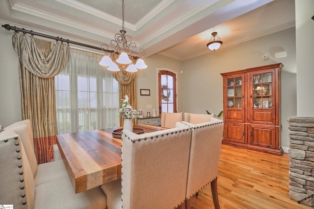 dining area with a notable chandelier, ornamental molding, a tray ceiling, and light wood-type flooring