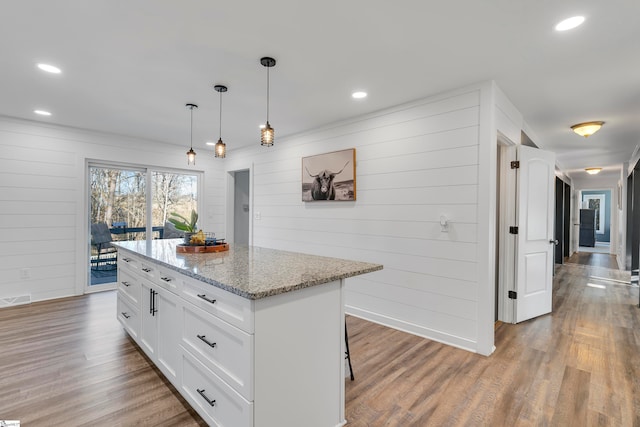 kitchen featuring hardwood / wood-style floors, a kitchen island, white cabinetry, pendant lighting, and light stone counters