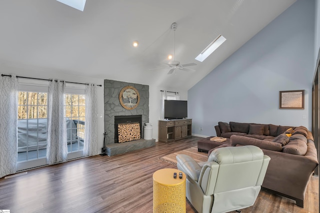 living room featuring a stone fireplace, ceiling fan, a skylight, high vaulted ceiling, and dark hardwood / wood-style flooring