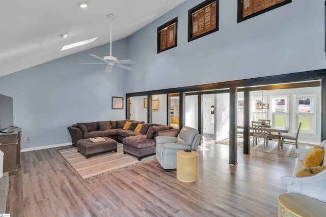 living room featuring hardwood / wood-style floors, high vaulted ceiling, a skylight, and ceiling fan