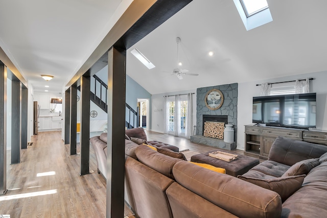 living room with a stone fireplace, high vaulted ceiling, light wood-type flooring, and ceiling fan